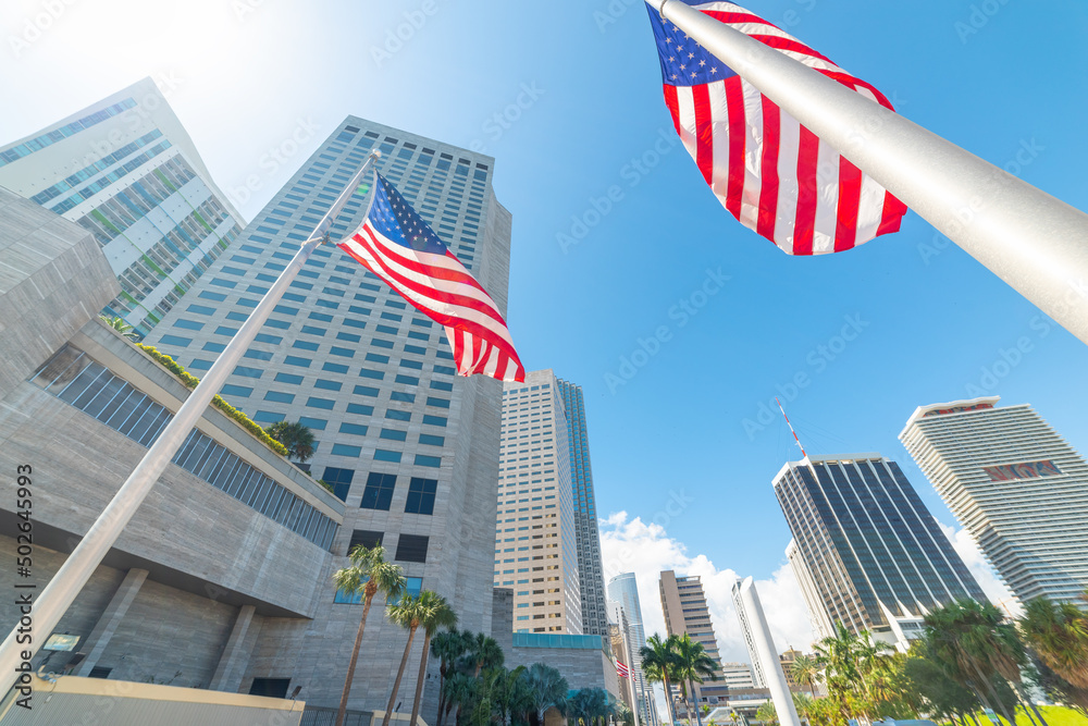 Skyscrapers and US flags in downtown Miami under a shining sun - obrazy, fototapety, plakaty 