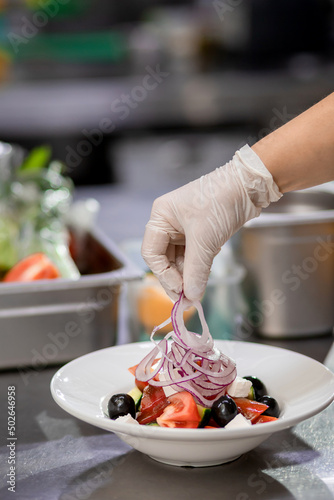 The chef in the kitchen imposes freshly chopped onions and prepares a Greek salad. Concept of сooking vegetarian salad
