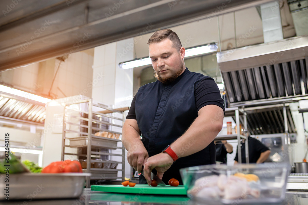 The chef in the kitchen cuts a tomato for the chicken dish The chef in the kitchen cuts a tomato for the chicken dish