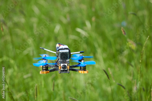 Wallpaper Mural Small racing drone also quad copter with blue propellers and a big battery, floats calmly over a beautiful meadow. View directly from the front. Depth of field. Natural. Torontodigital.ca