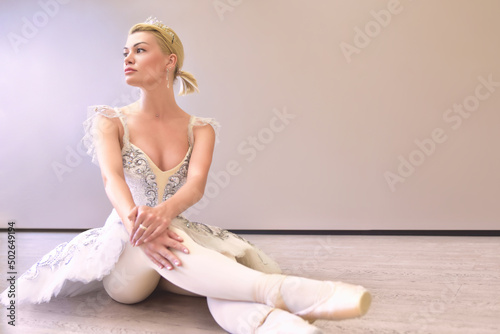 amazing woman ballerina sitting in a dance studio over beige wall background isolated