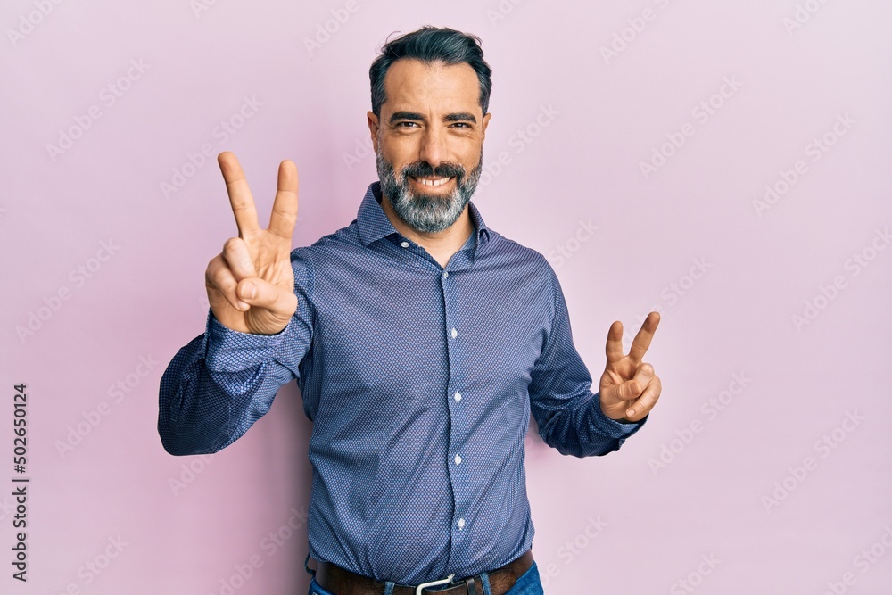 Middle age man with beard and grey hair wearing business clothes smiling looking to the camera showing fingers doing victory sign. number two. Middle age man with beard and grey hair wearing business clothes smiling looking to the camera showing fingers doing victory sign. number two.