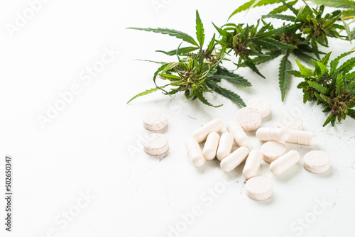 CBD pills and green leaf at white table. Alternative medicine. Sedative, antibiotic, antioxidant using cannabis products.