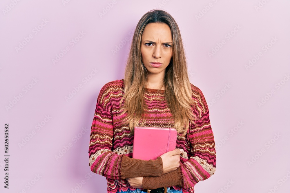 Beautiful hispanic woman hugging book skeptic and nervous, frowning upset because of problem. negative person. Beautiful hispanic woman hugging book skeptic and nervous, frowning upset because of problem. negative person.