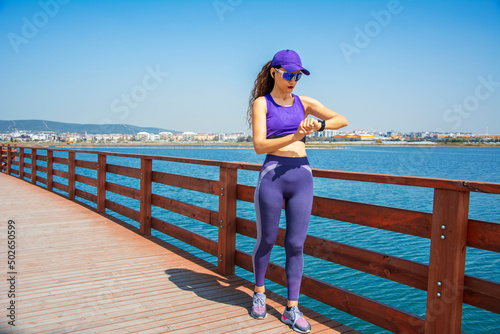 Woman adjusting her smartwatch before running on bridge by lake