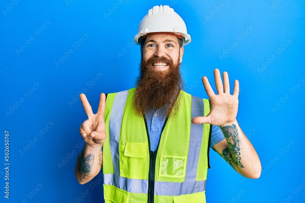Redhead man with long beard wearing safety helmet and reflective jacket showing and pointing up with fingers number seven while smiling confident and happy.