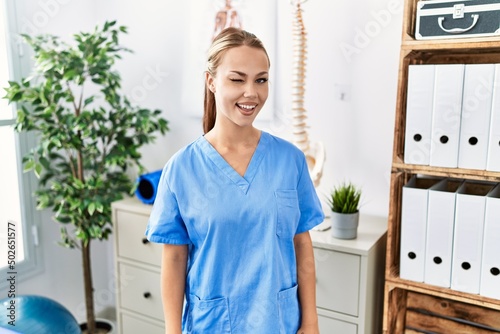 Young caucasian woman working at pain recovery clinic winking looking at the camera with sexy expression  cheerful and happy face.
