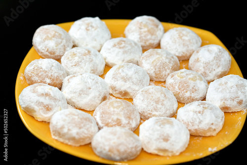 yellow plate of traditional Arabic cookies for celebration of Islamic holidays of El-Fitr feast, Egyptian Kahk covered with powdered sugar and stuffed nuts and hazelnuts and Malban isolated on black photo