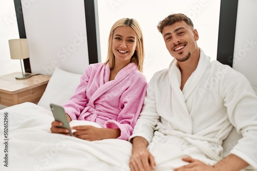 Young caucasian couple smiling happy using smartphone sitting on the bed at home. © Krakenimages.com