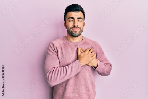 Tableau sur toile Young hispanic man wearing casual clothes smiling with hands on chest, eyes closed with grateful gesture on face