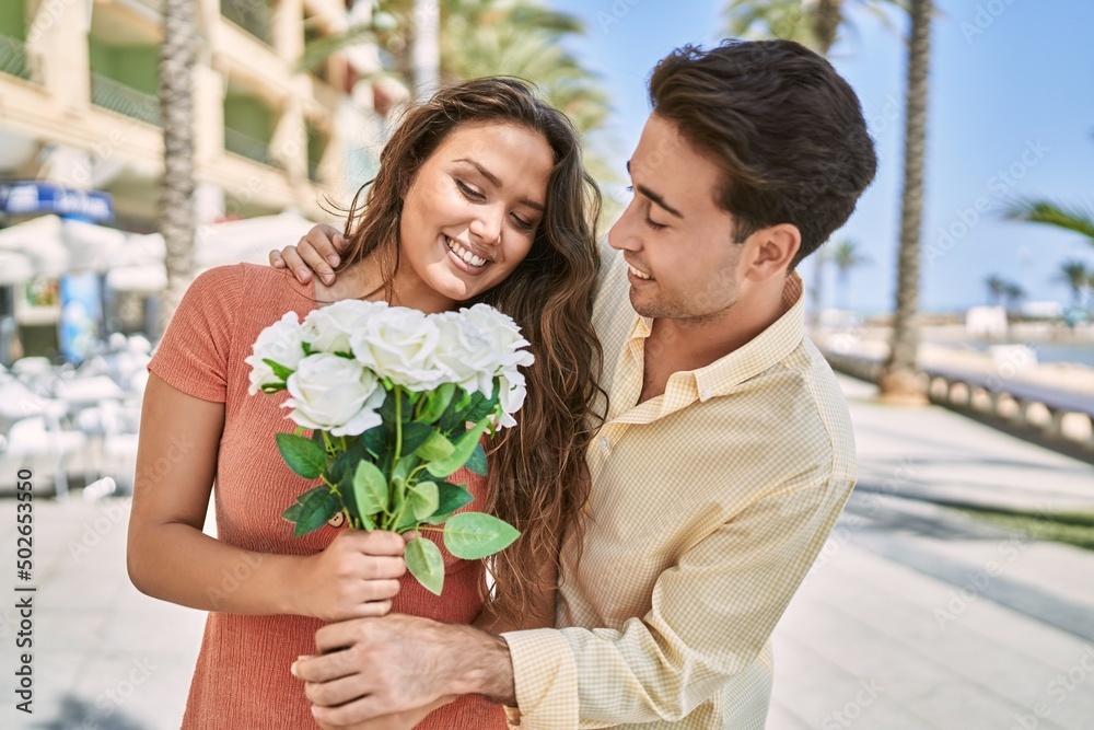 Naklejka premium Man and woman couple holding bouquet of flowers hugging each other at seaside