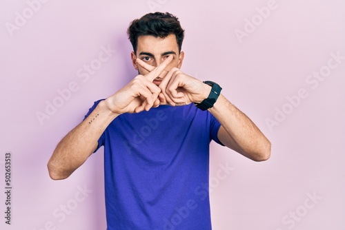 Young hispanic man wearing casual t shirt rejection expression crossing fingers doing negative sign