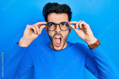 Wallpaper Mural Young hispanic man wearing glasses angry and mad screaming frustrated and furious, shouting with anger looking up. Torontodigital.ca