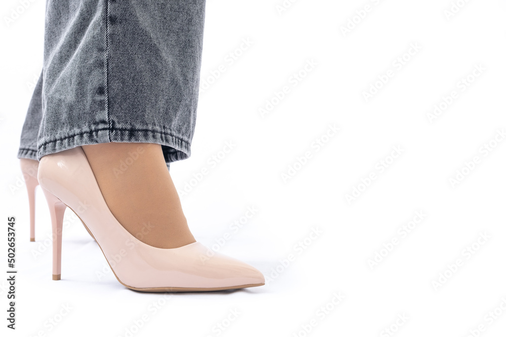 Women's legs in elegant patent leather high-heeled beige shoes. Gray wide leg jeans. Side view Women's legs in elegant patent leather high-heeled beige shoes. Gray wide leg jeans. Side view