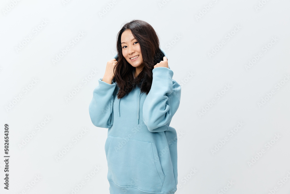 Fashionable smiling happy cute Asian young female in blue sweatshirt puts on the hood posing isolated on over white studio background. The best offer for ad. Fashion New Collection Ad concept Fashionable smiling happy cute Asian young female in blue sweatshirt puts on the hood posing isolated on over white studio background. The best offer for ad. Fashion New Collection Ad concept