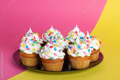cupcakes with white frosting and colorful sprinkles placed on a round tray  set against a dual-color background.