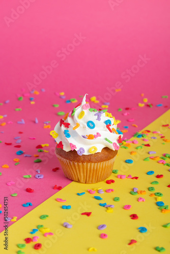 Decorated cupcake with a candle amidst scattered confetti on a dual-tone backdrop.