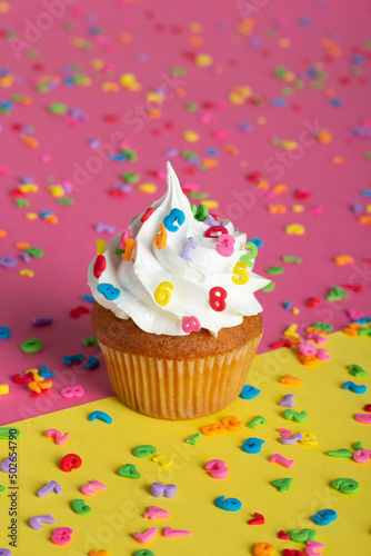 Celebration-themed cupcake with a candle  positioned on a background scattered with multicolored pieces.
