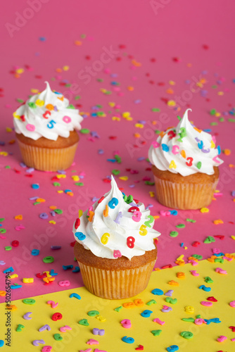 Cupcakes with creamy topping and colorful sprinkles on a two-tone pink and yellow backdrop.