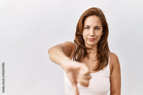 Middle age hispanic woman standing over isolated background looking unhappy and angry showing rejection and negative with thumbs down gesture. bad expression.