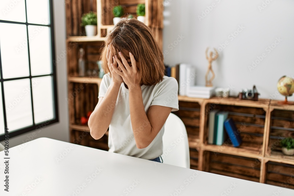 Young caucasian girl wearing casual clothes sitting on the table at home with sad expression covering face with hands while crying. depression concept.