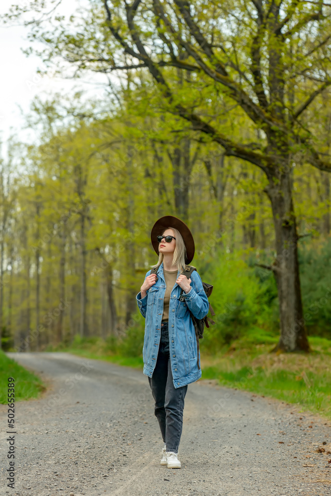 Woman with backpack walking on road in forest in spring time Woman with backpack walking on road in forest in spring time
