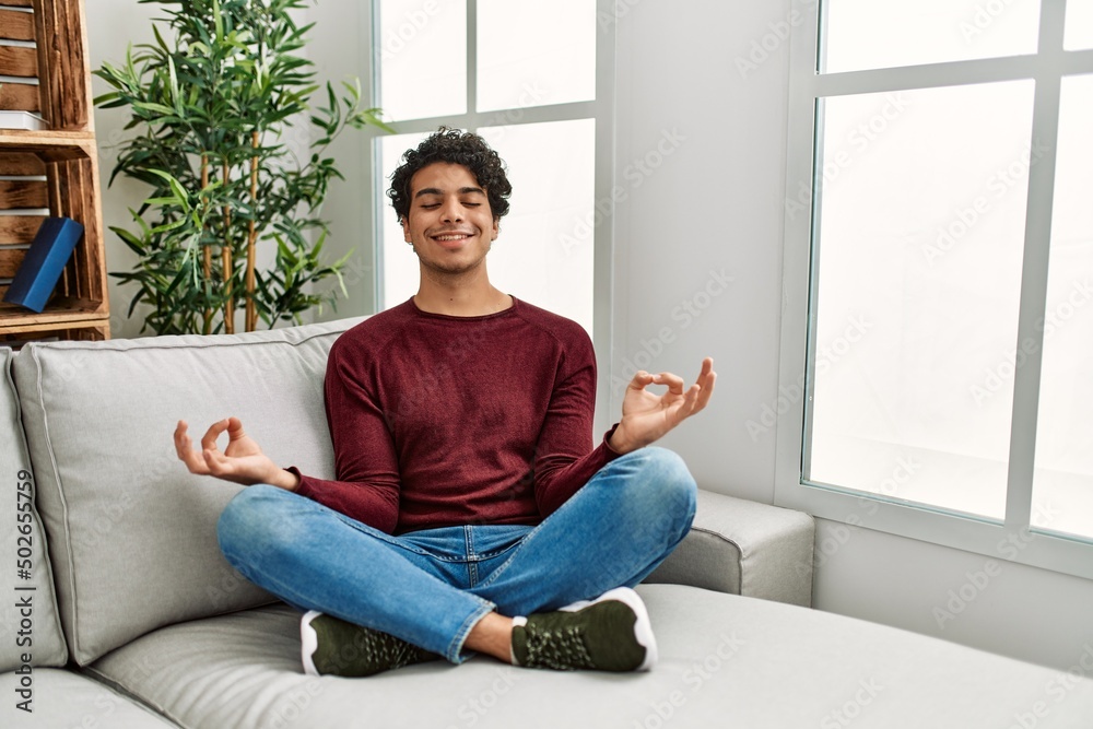 Young hispanic man meditation doing yoga sitting on the sofa at home. Young hispanic man meditation doing yoga sitting on the sofa at home.