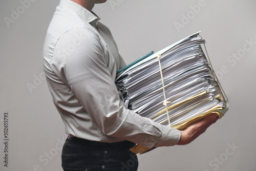  Impiegato con fatica tiene tra le braccia un enorme fascicolo di documenti ed uno smartphone 