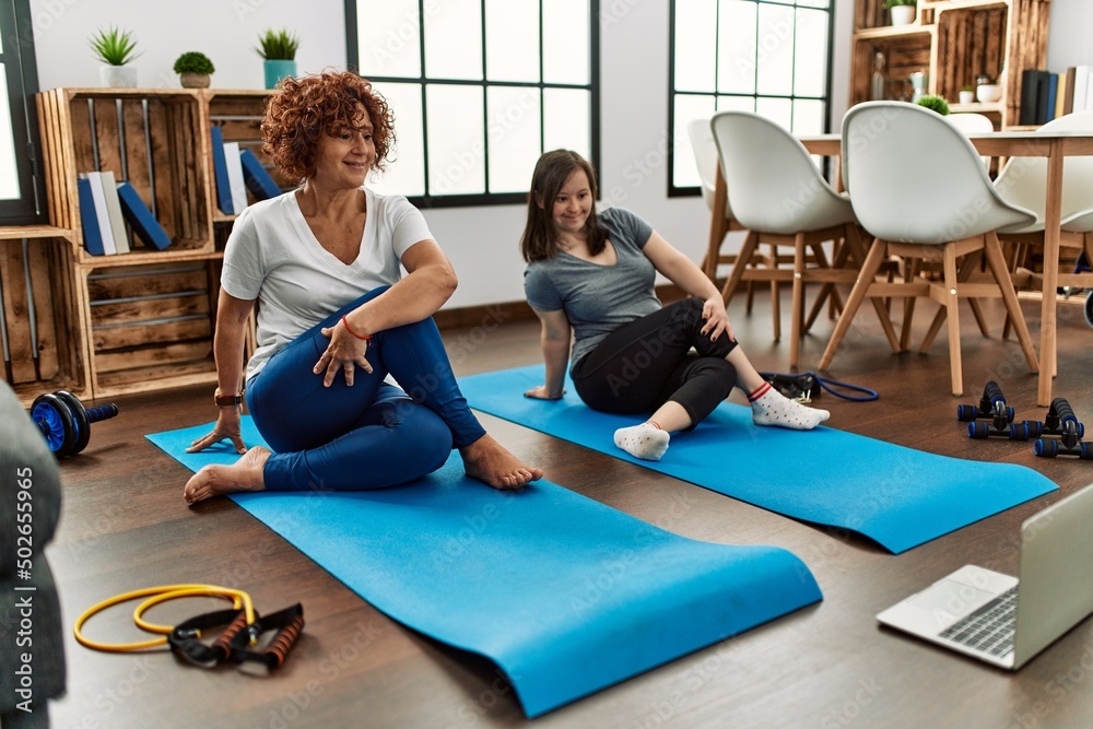 Mature mother and down syndrome daughter doing exercise at home. Stretching at the living room