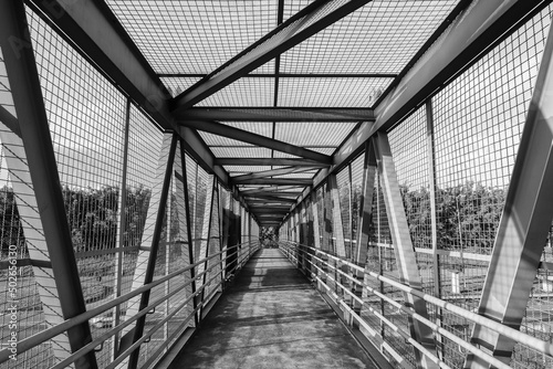 Pedestrian bridge in metallic structure with railings over the highway. D. Pedro I highway, Atibaia, Brazil. Black and white photography. 
