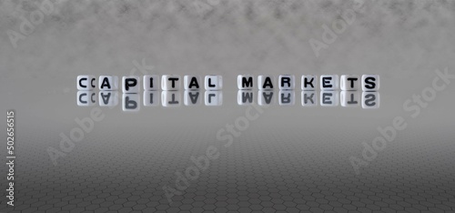 capital markets word or concept represented by black and white letter cubes on a grey horizon background stretching to infinity