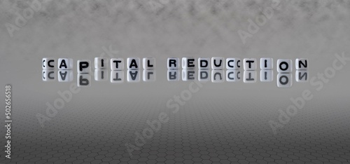 capital reduction word or concept represented by black and white letter cubes on a grey horizon background stretching to infinity