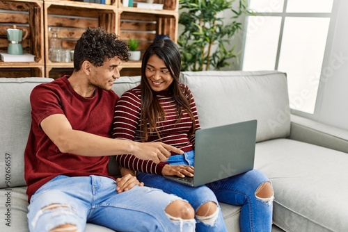 Young latin couple smiling happy using laptop sitting on the sofa at home.