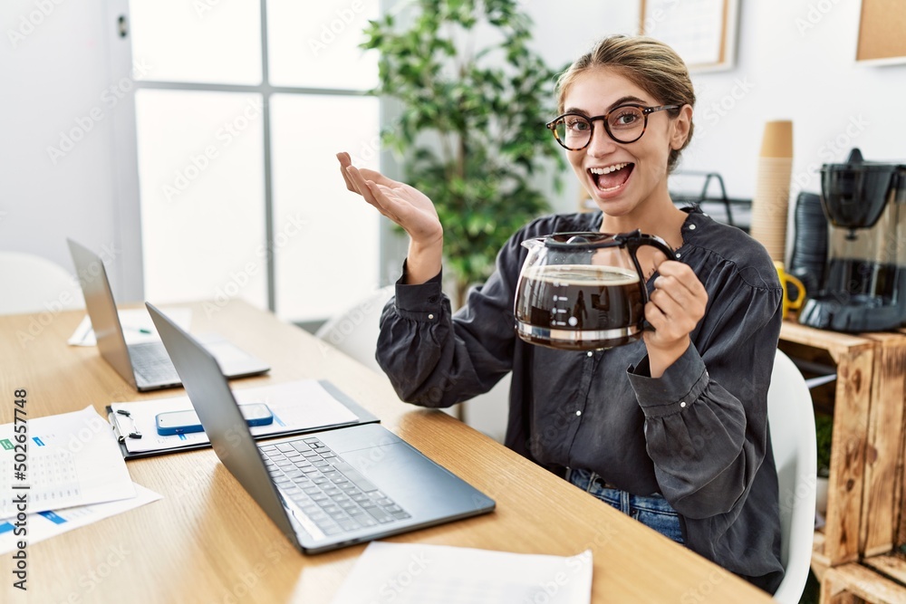 Young blonde woman working at the office holding coffee pot celebrating achievement with happy smile and winner expression with raised hand Young blonde woman working at the office holding coffee pot celebrating achievement with happy smile and winner expression with raised hand