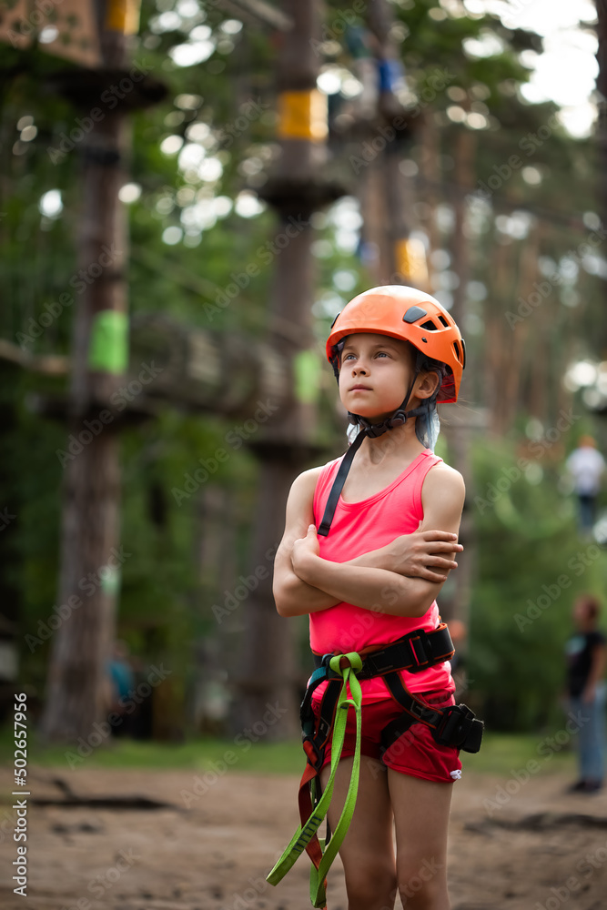 Portrait of little serious girl in helmet and harness in the sky rope park in summer