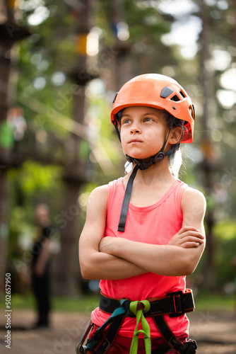 Portrait of little serious girl in helmet and harness in the sky rope park in summer