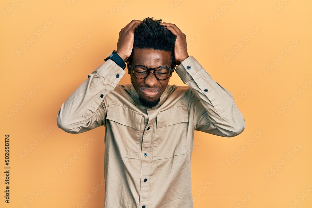 Young african american man wearing casual clothes and glasses suffering from headache desperate and stressed because pain and migraine. hands on head. Young african american man wearing casual clothes and glasses suffering from headache desperate and stressed because pain and migraine. hands on head.