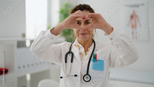 Middle age hispanic woman wearing doctor uniform doing heart symbol with hands at clinic © Krakenimages.com