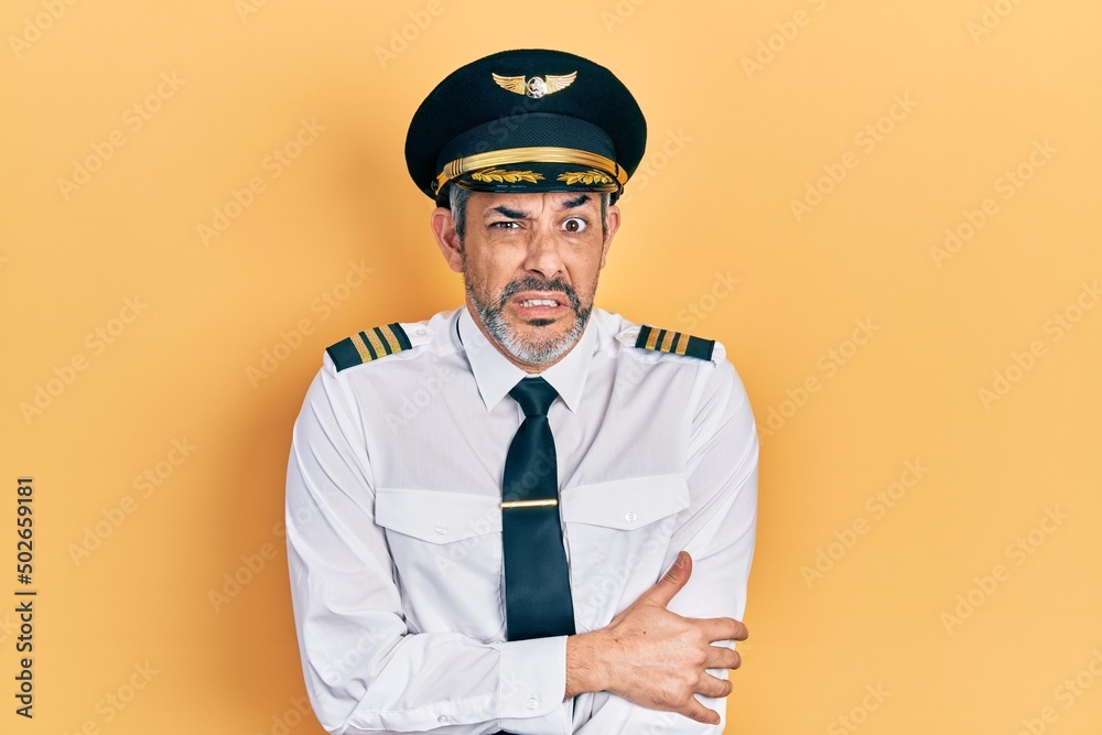 Handsome middle age man with grey hair wearing airplane pilot uniform shaking and freezing for winter cold with sad and shock expression on face Handsome middle age man with grey hair wearing airplane pilot uniform shaking and freezing for winter cold with sad and shock expression on face