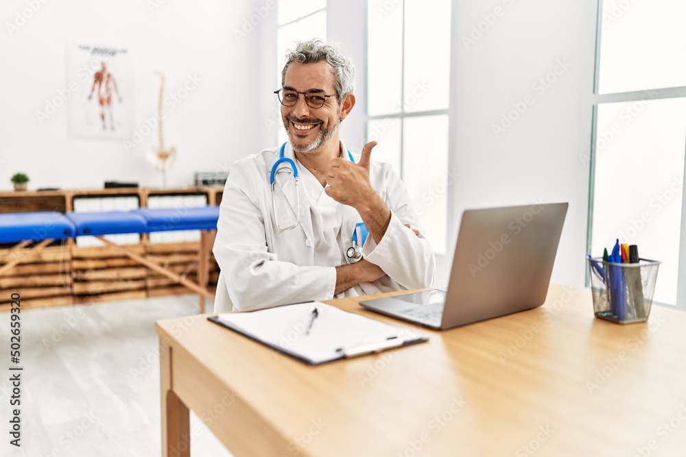 Middle age hispanic therapist man working at pain recovery clinic with laptop smiling happy and positive, thumb up doing excellent and approval sign Middle age hispanic therapist man working at pain recovery clinic with laptop smiling happy and positive, thumb up doing excellent and approval sign