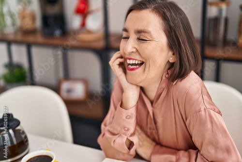 Middle age woman smiling confident sitting on table at home