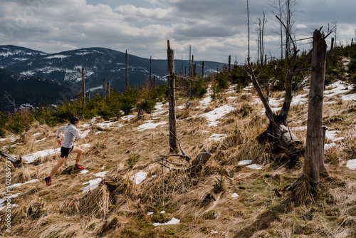 Fototapeta Naklejka Na Ścianę i Meble -  Trail male runner is running up a steep trail in the Beskidy mountains. There is some snow on the route.