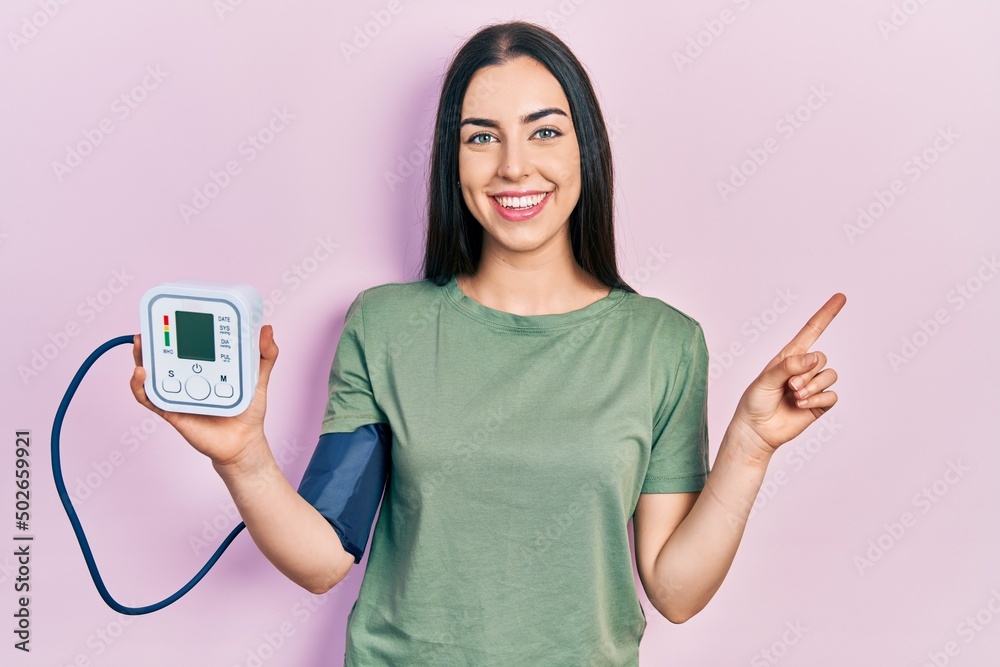 Beautiful woman with blue eyes using glucose meter smiling happy pointing with hand and finger to the side Beautiful woman with blue eyes using glucose meter smiling happy pointing with hand and finger to the side