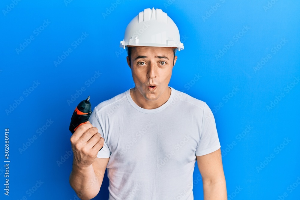 Handsome young man holding screwdriver wearing hardhat scared and amazed with open mouth for surprise, disbelief face Handsome young man holding screwdriver wearing hardhat scared and amazed with open mouth for surprise, disbelief face