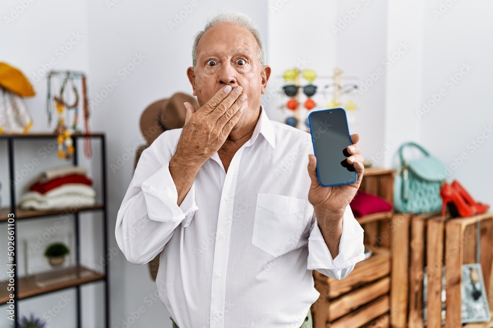 Senior man holding smartphone at retail shop covering mouth with hand, shocked and afraid for mistake. surprised expression Senior man holding smartphone at retail shop covering mouth with hand, shocked and afraid for mistake. surprised expression