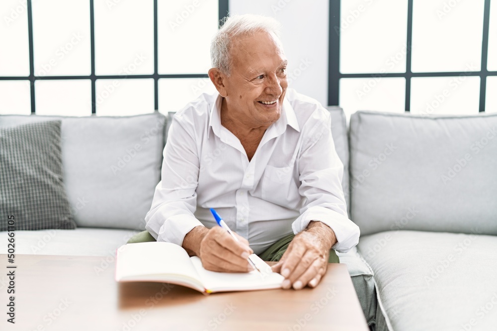 Senior man writing on book sitting on sofa at home