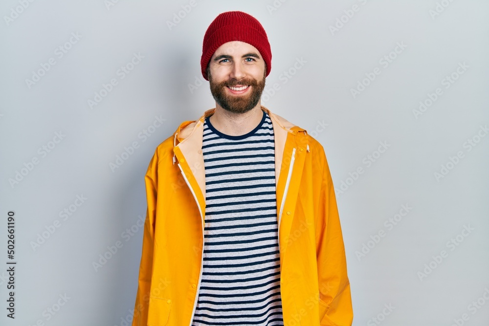 Caucasian man with beard wearing yellow raincoat with a happy and cool smile on face. lucky person.