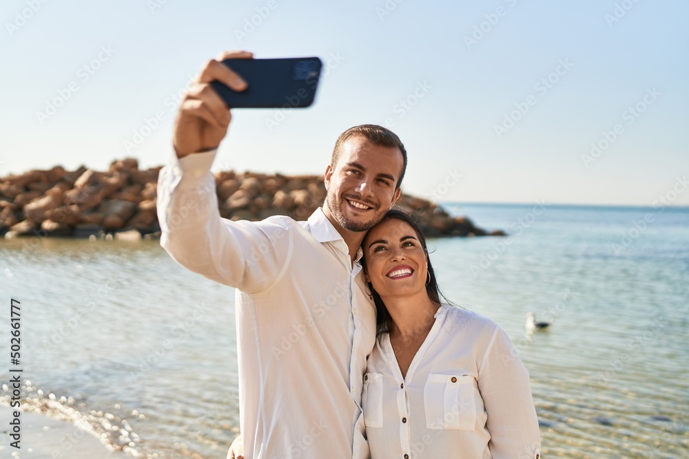 Man and woman couple hugging each other make selfie by the smartphone standing at seaside Man and woman couple hugging each other make selfie by the smartphone standing at seaside