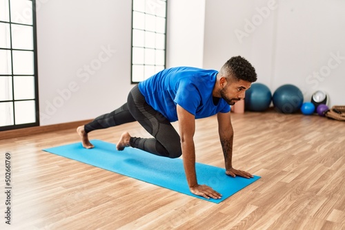 Handsome hispanic man doing exercise and stretching on yoga mat, practicing flexibility and training at the gym