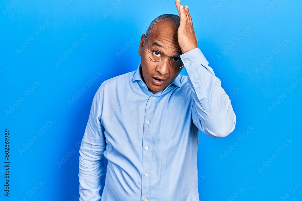 Middle age latin man wearing casual clothes and glasses surprised with hand on head for mistake, remember error. forgot, bad memory concept.